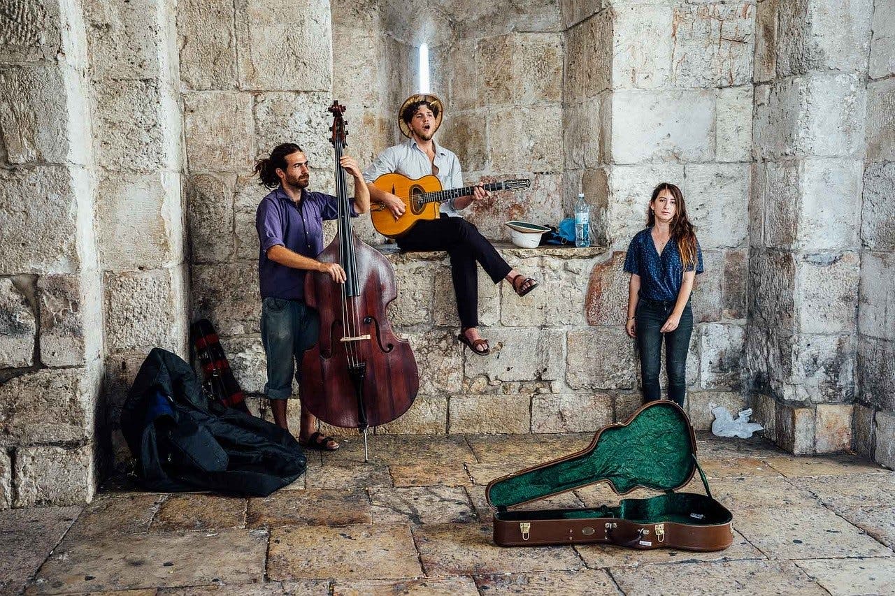 A group of musicians including a bassist, guitarist, and singer, relax in an old stone building.