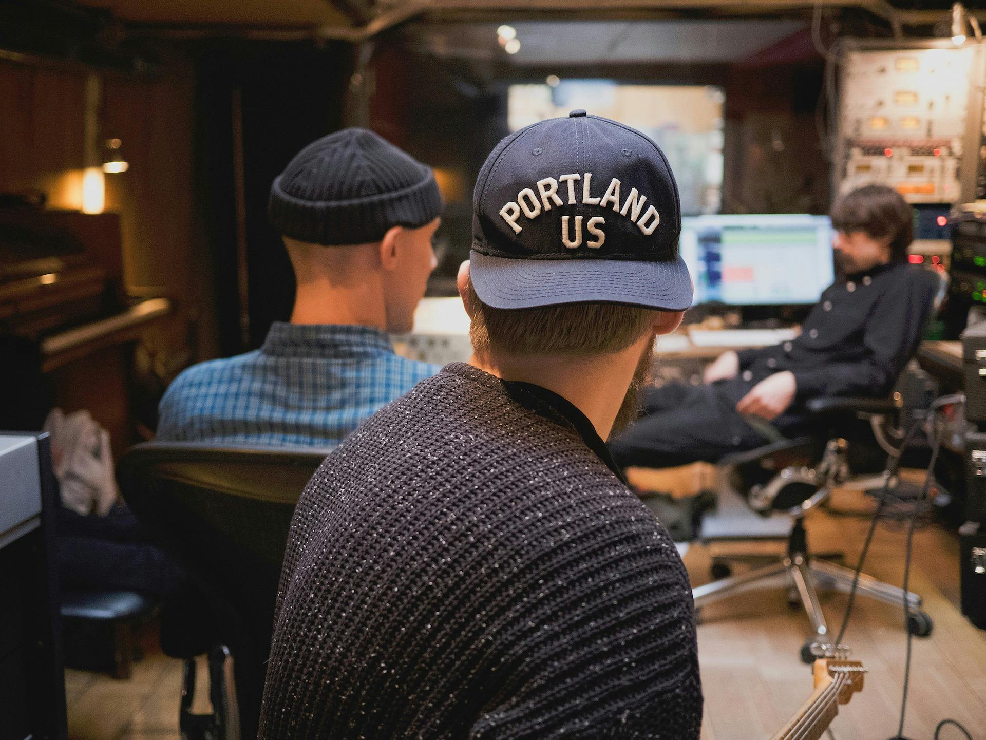 Three music producers collaborating in a studio surrounded by instruments.